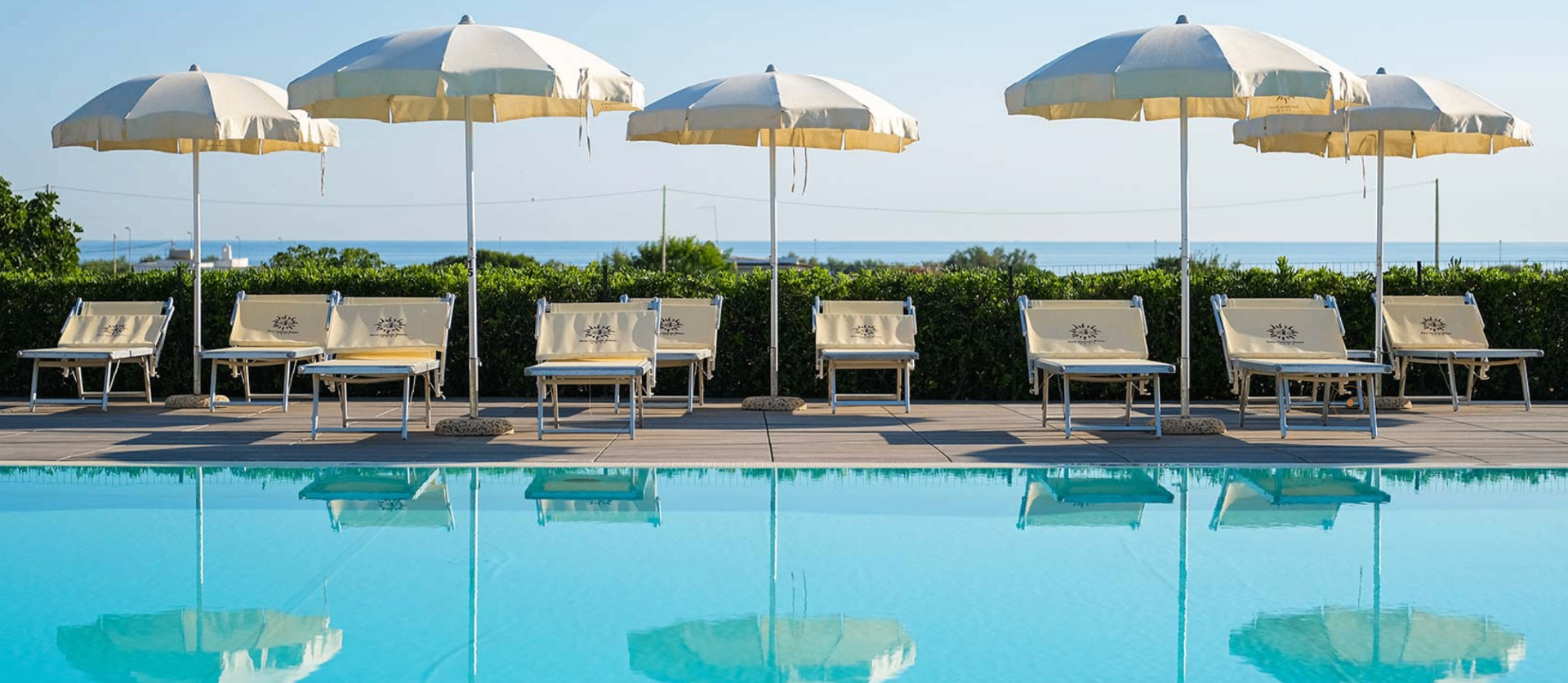 Lettini e ombrelloni a bordo piscina con vista sul mare